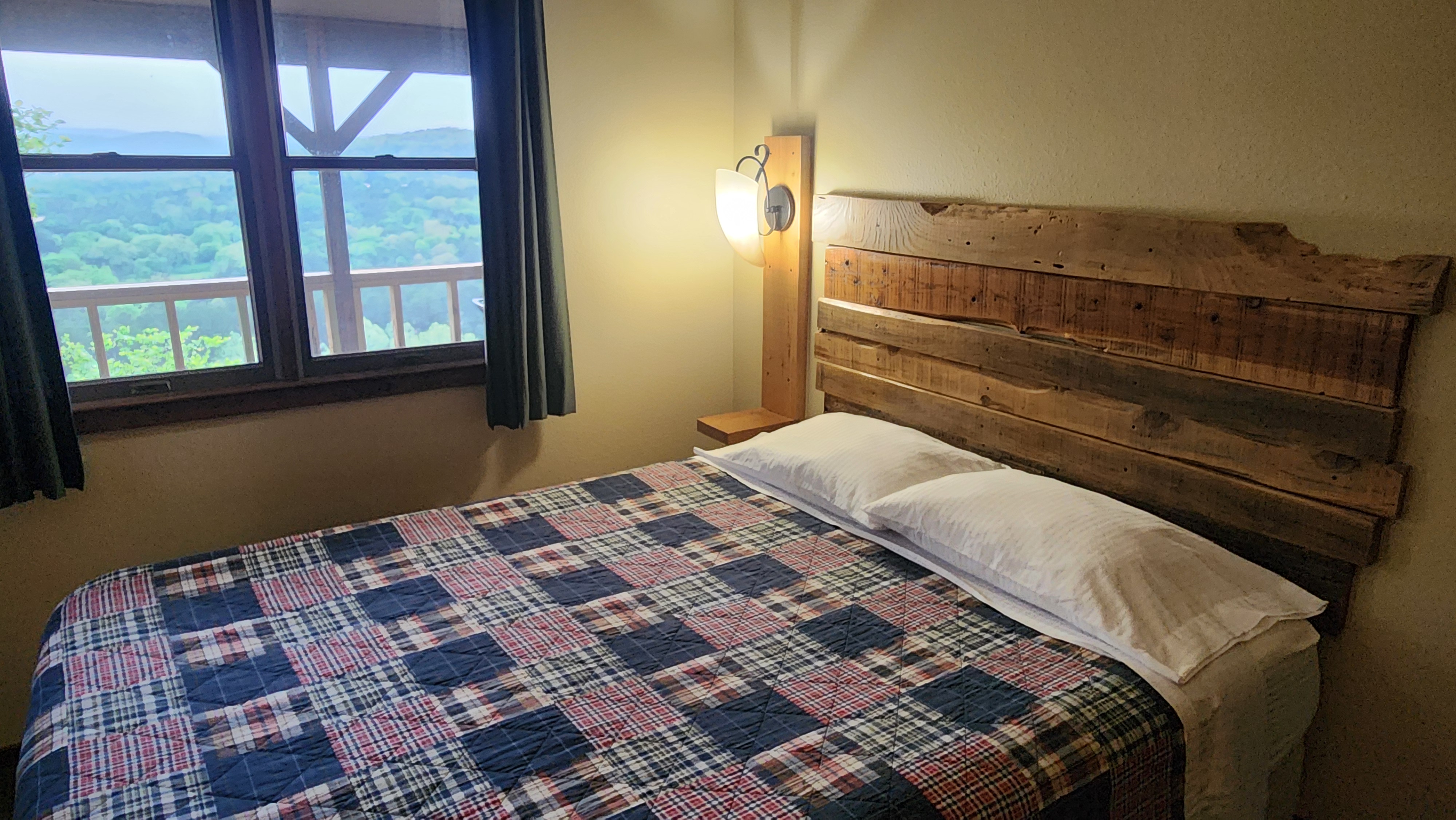Valley View master bedroom with queen bed, plaid quilt, wood plank headboard, and White River valley view window