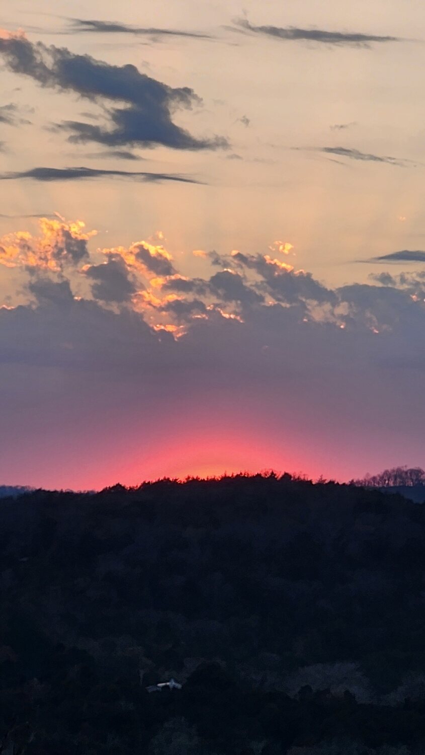 Deep red sunset glow on the horizon beneath storm clouds over the Ozark ridgeline