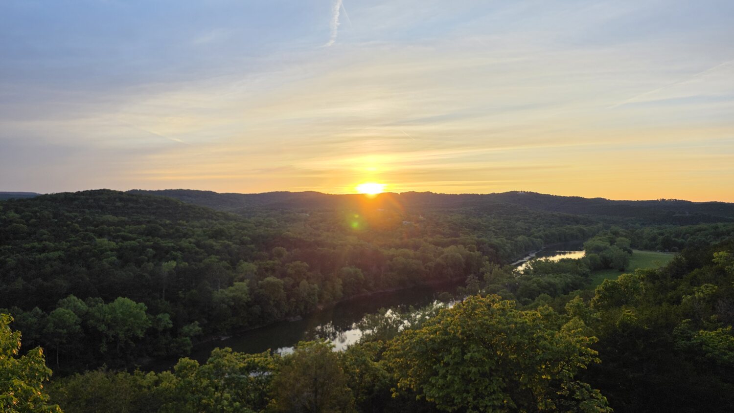 Sun setting behind layered Ozark ridgelines in shades of gold and green