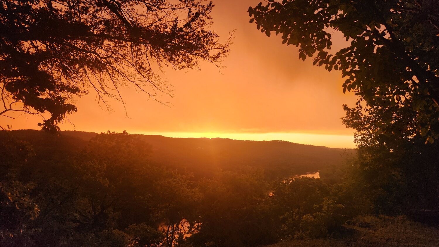 Golden sunburst breaking through silhouetted trees above the Ozark Mountains at dusk